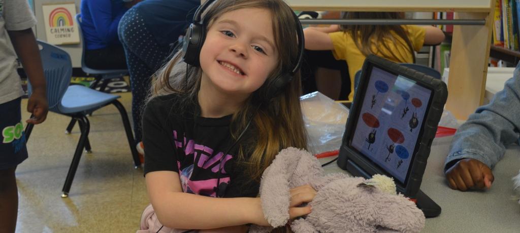 girl wearing headphones and working on an iPad with her pink bunny