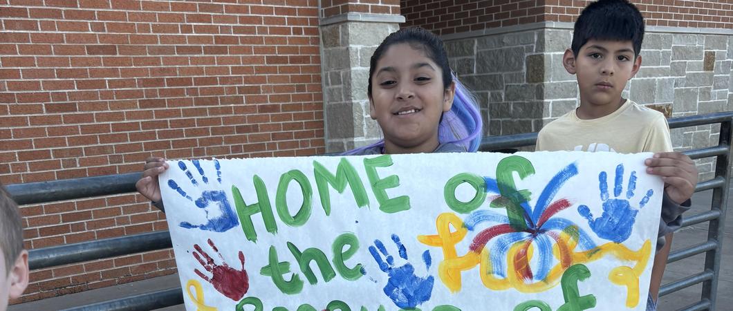 A child holding a banner that says Home of the Free because of the Brave.