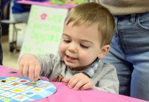 Toddler happily places stickers on a circular board at a colorful table.