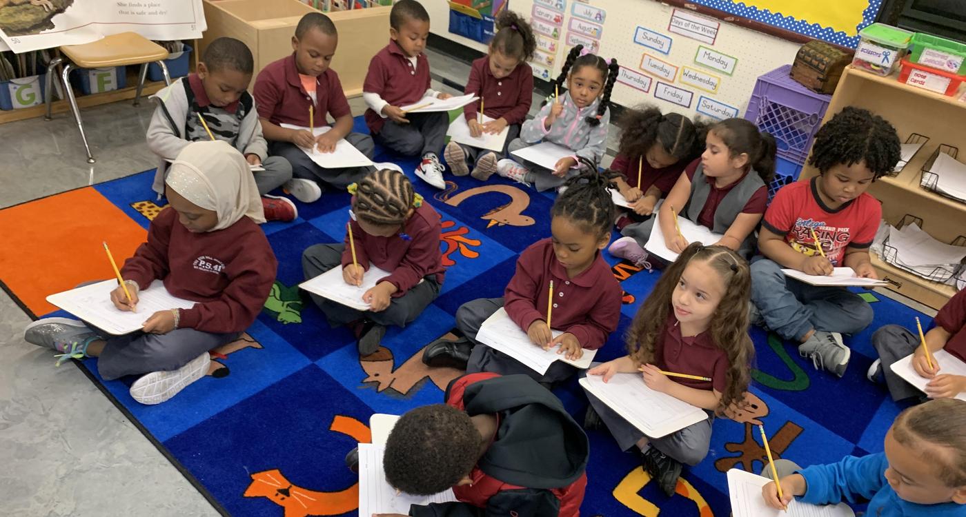 Students engaged in writing on a colorful classroom rug.
