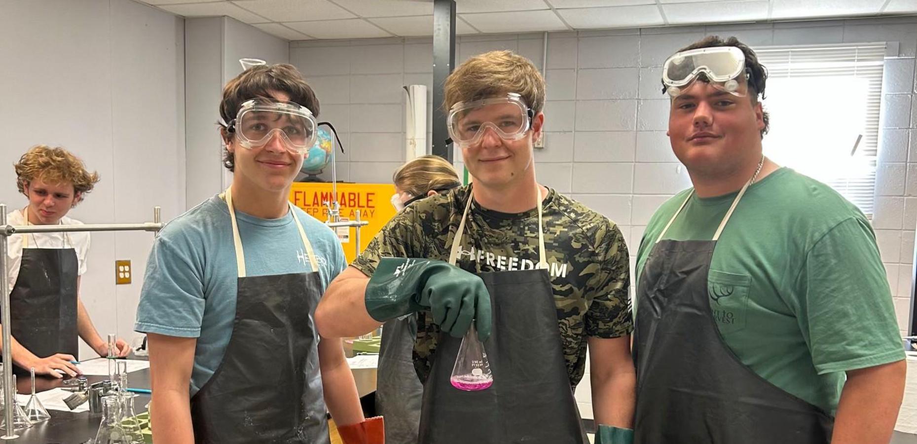 Three students in experiment gear hold a flask during a chemistry class.