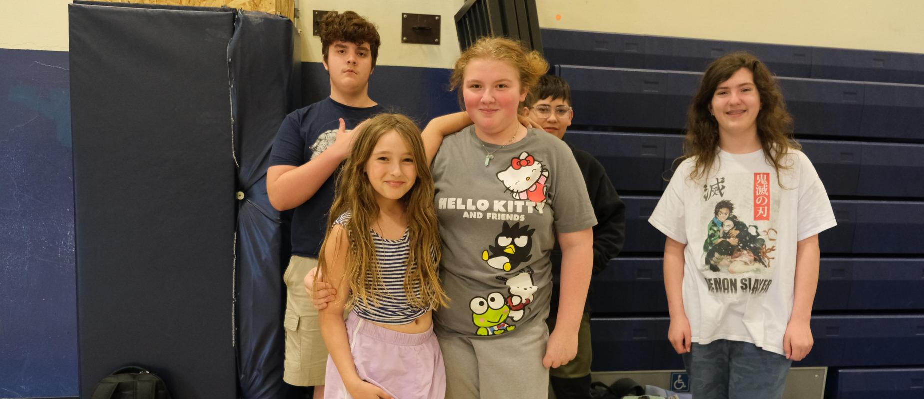 A group of five children posing together in a gym, smiling and enjoying their time.