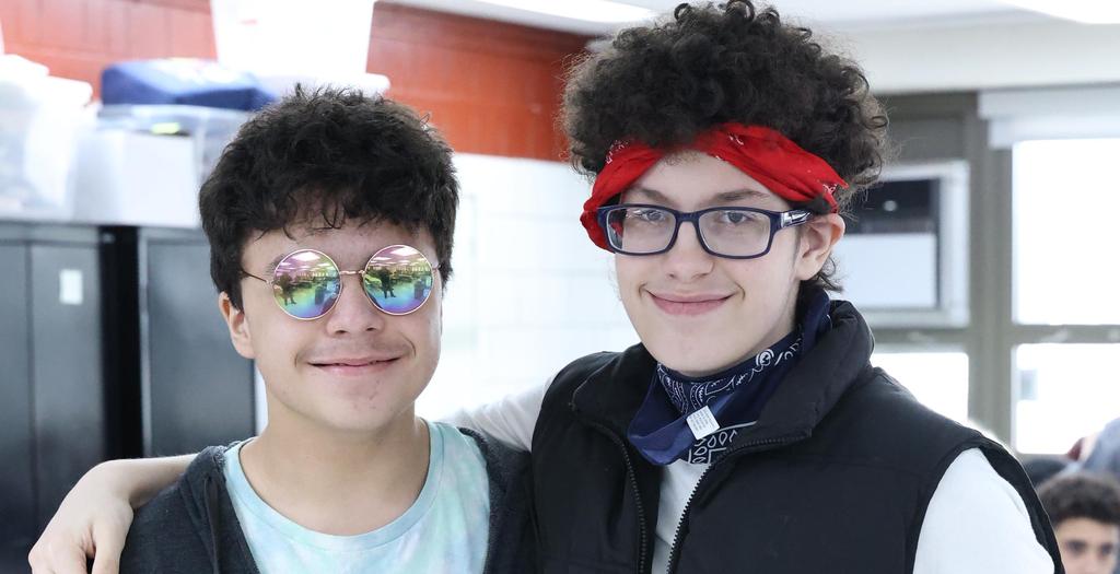 Two boys with arms around each other. One with a red bandanna on his head the other boy with sunglasses.