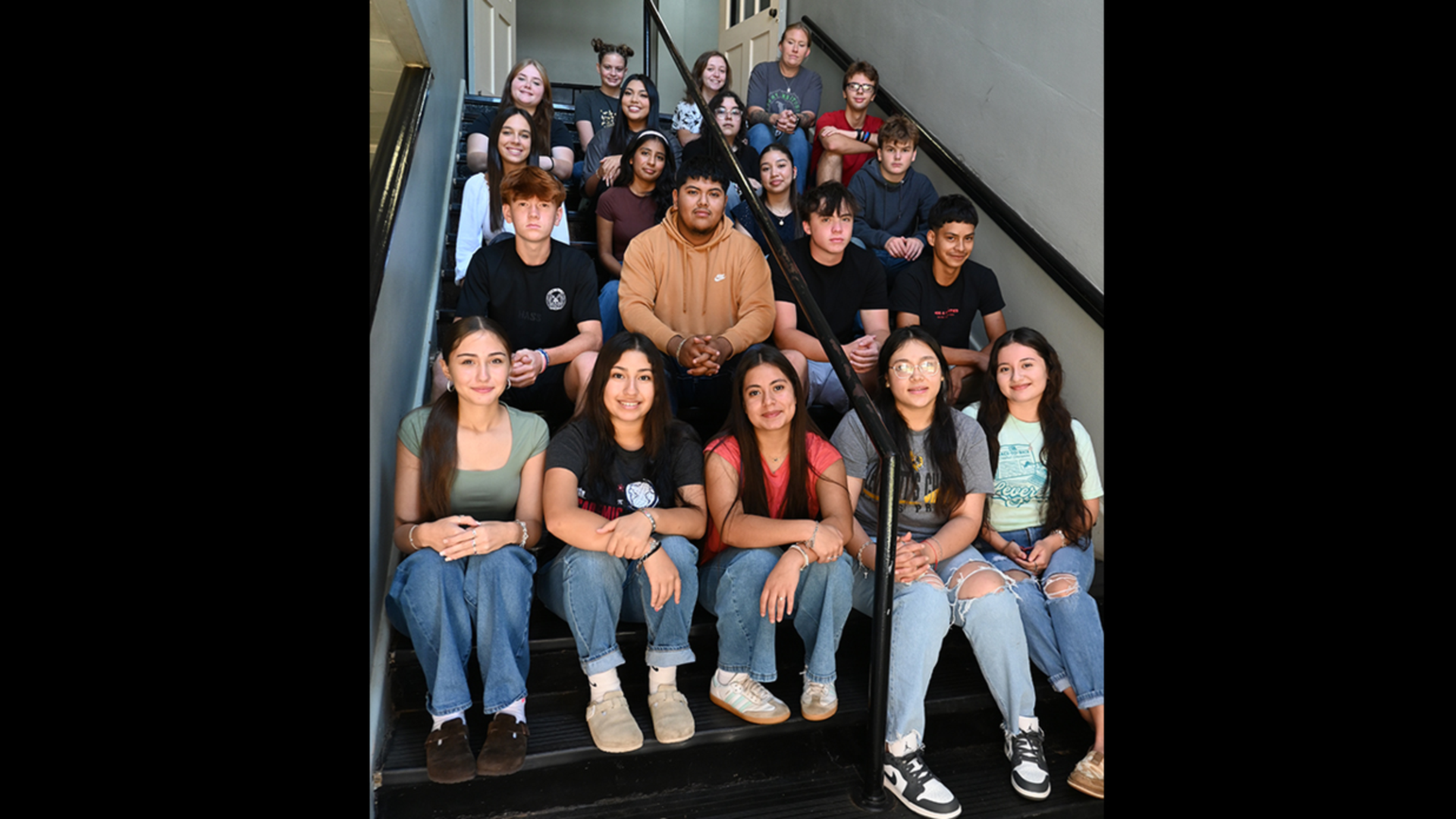 A diverse group of students sitting on stairs in a school building.