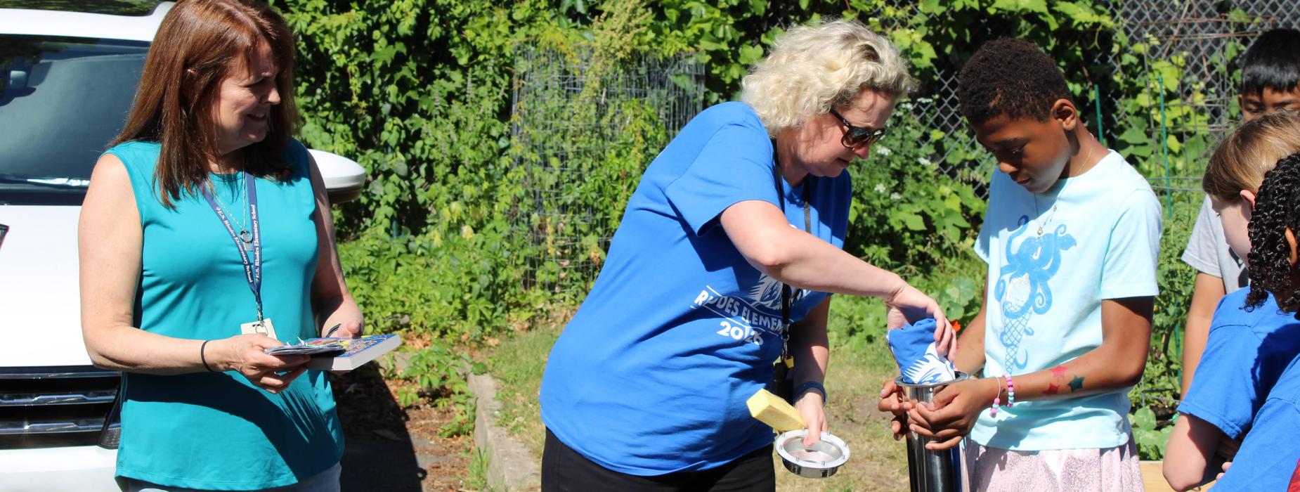 Principal Heather Breton and 5th gr. teacher Susan Weber help a student place items into the silver time capsule to be opened in seven years when they are seniors.