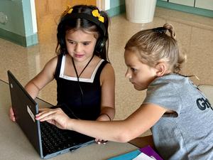Two elementary school students look carefully at a laptop screen