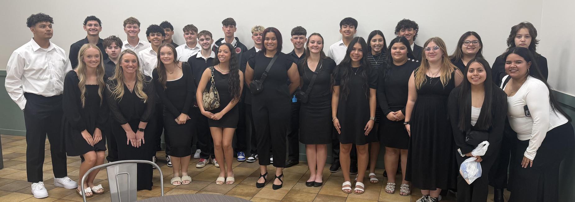 A large group of students in black attire poses together indoors.