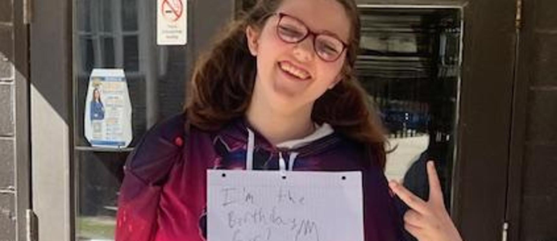 Person wearing a colorful sweatshirt holding a sign outdoors.
