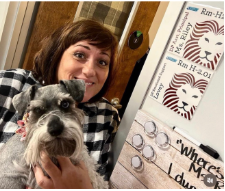 Ms. Riley holding her dog, Lovey, up next to her room plate