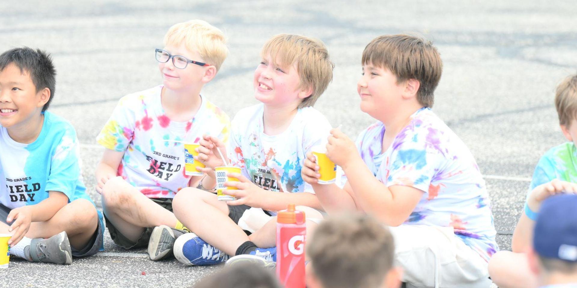 Group of children sitting together, enjoying snacks and laughing at an outdoor event.