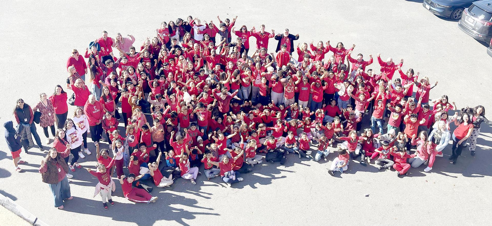 A large group of people in red shirts joyfully posing together outdoors.