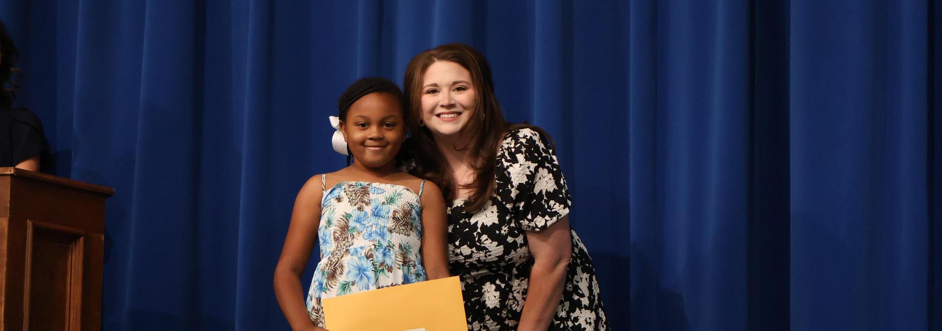 Student smiles with teacher at the third grade award assembly.