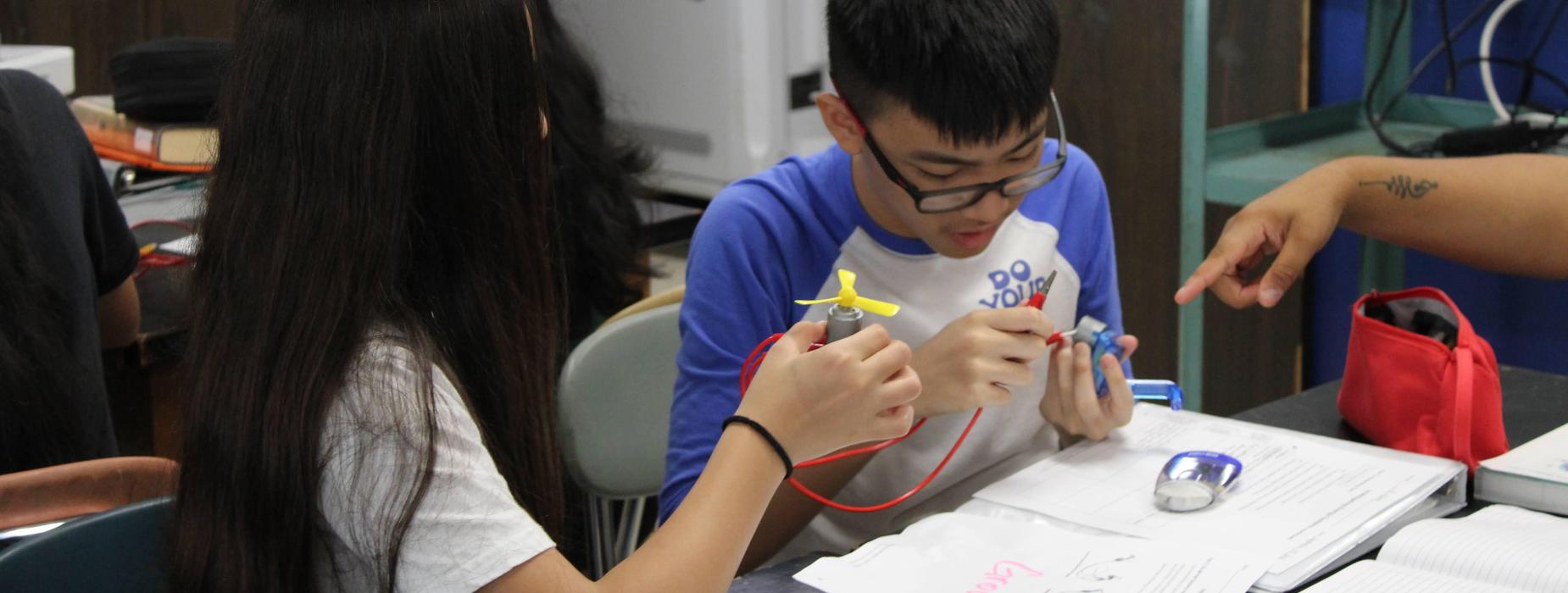 Two middle school students working with batteries and circuits to make a fan spin.