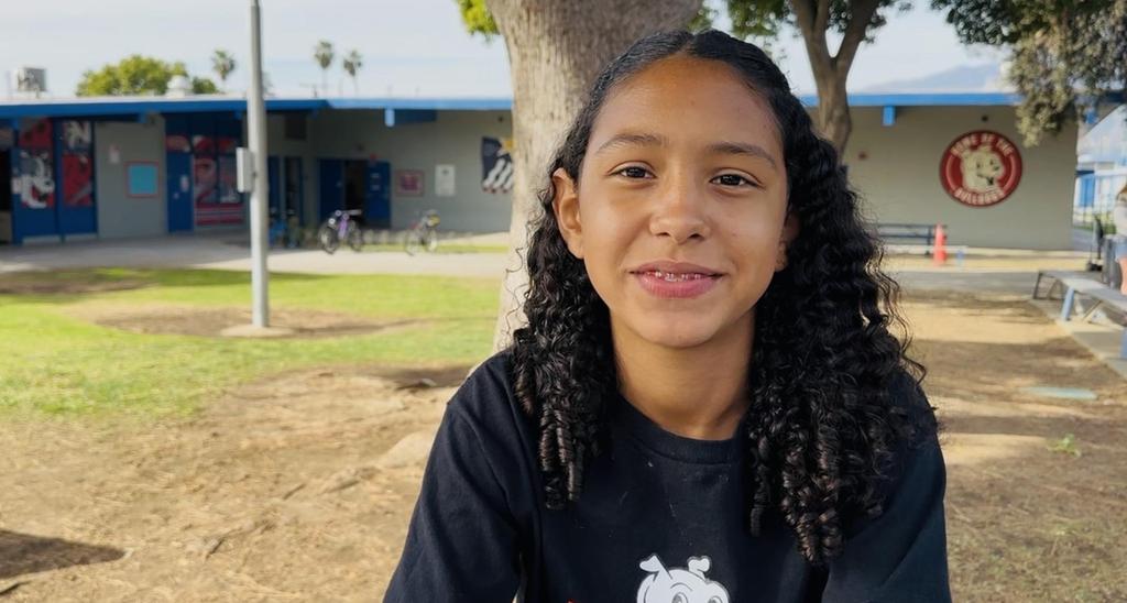 Young girl smiles outdoors near a school.