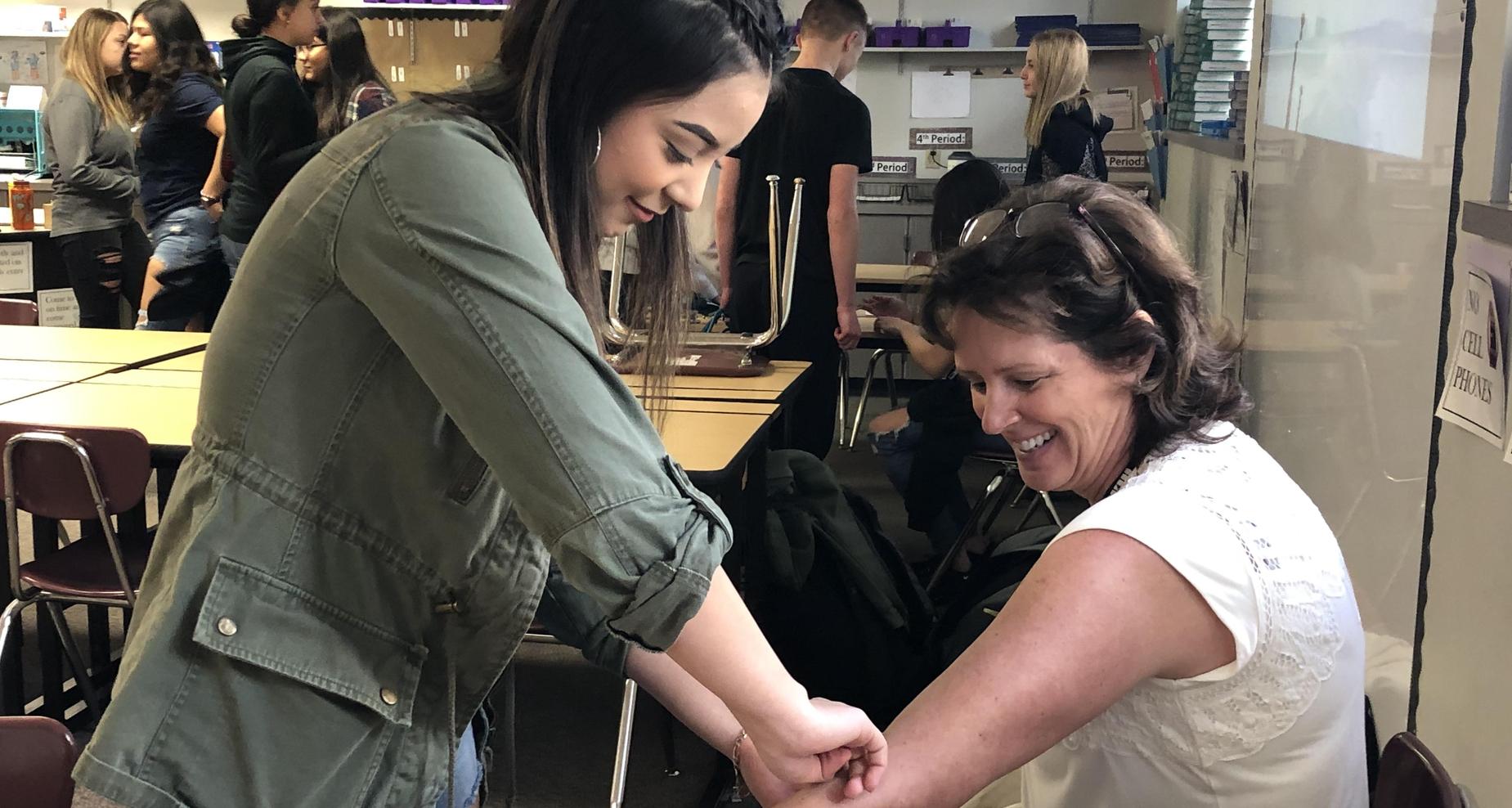 High school students checking teacher's blood pressure.