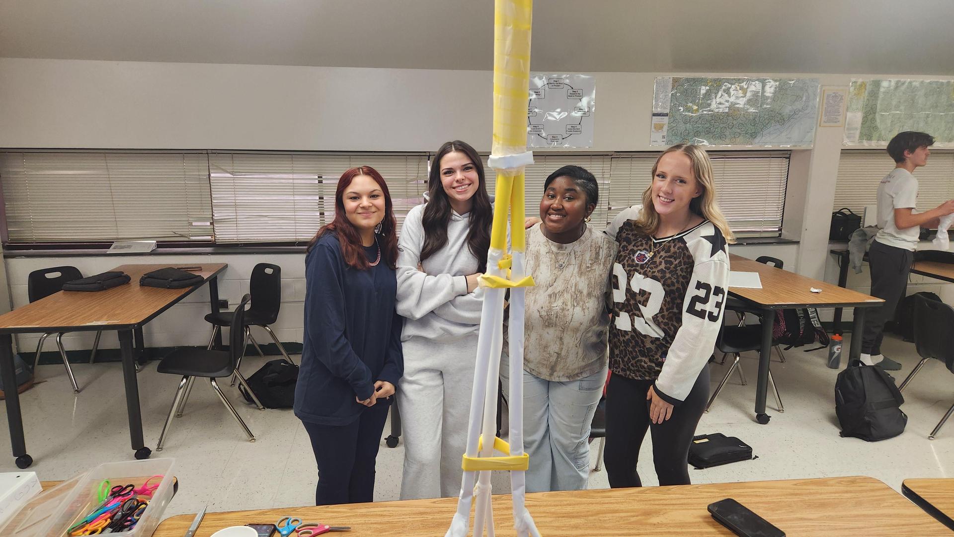 Four students posing together with a completed yellow and white tower.