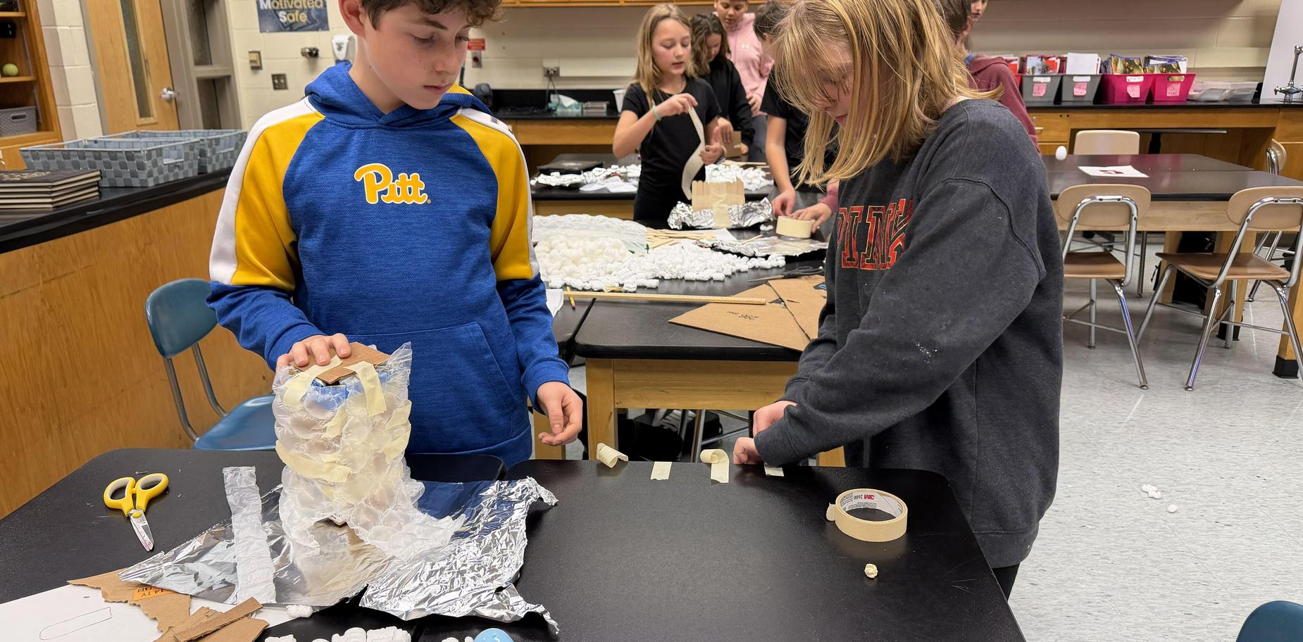 Students working on a crafting project with various materials at tables.