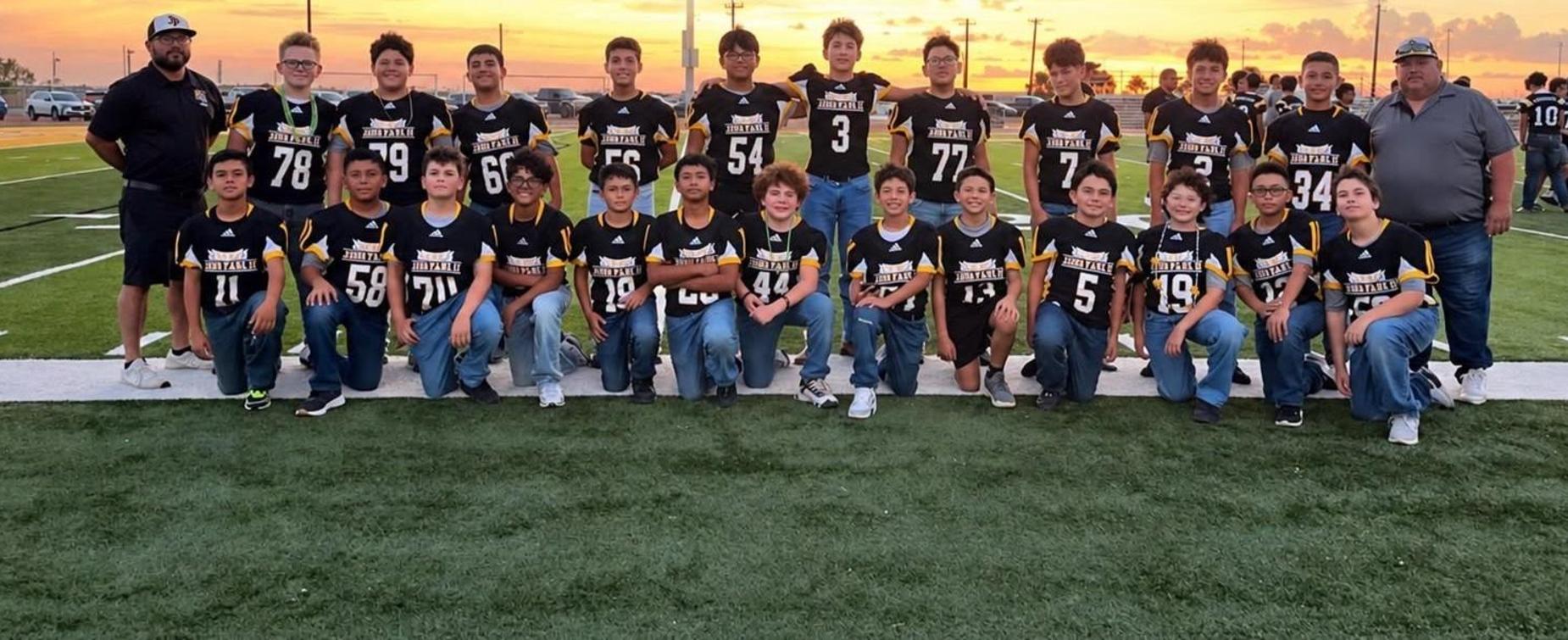 Group of young football players posing on a field at sunset.
