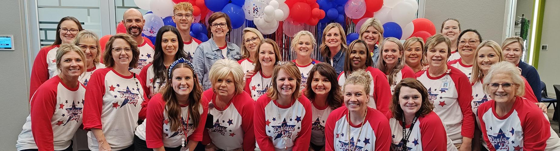 Group of smiling individuals wearing matching red and white shirts with stars.