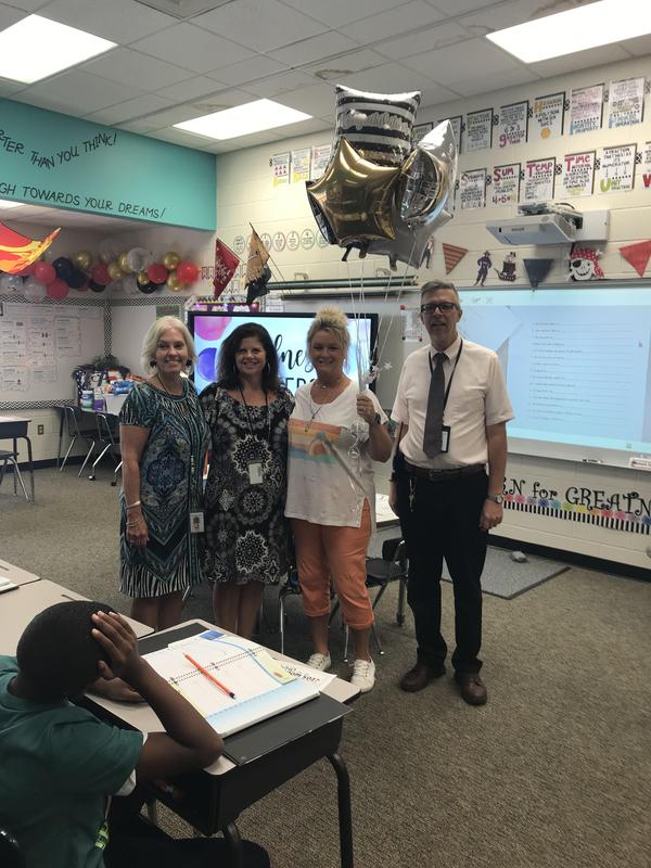 Amy Warrell and three other adults in front of classroom. Amy is holding balloons.
