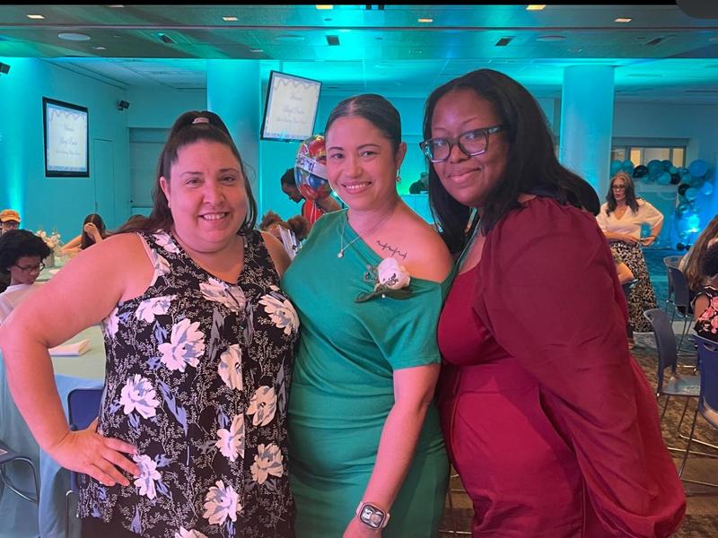 Three women standing next to each other in dresses for award ceremony.