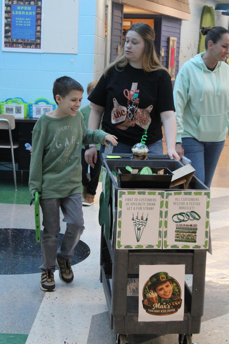 Student is walking down the hallway pushing coffee cart with an aide