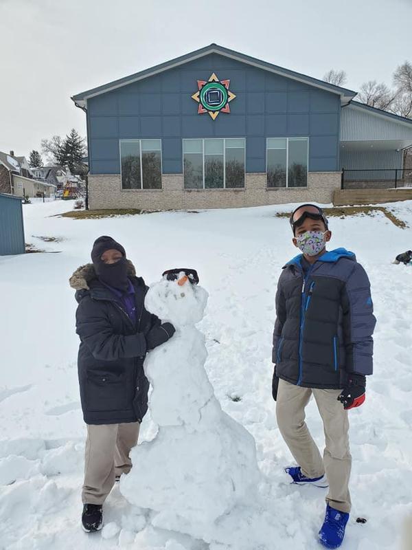 Image shows two scholars standing outside with a snowman