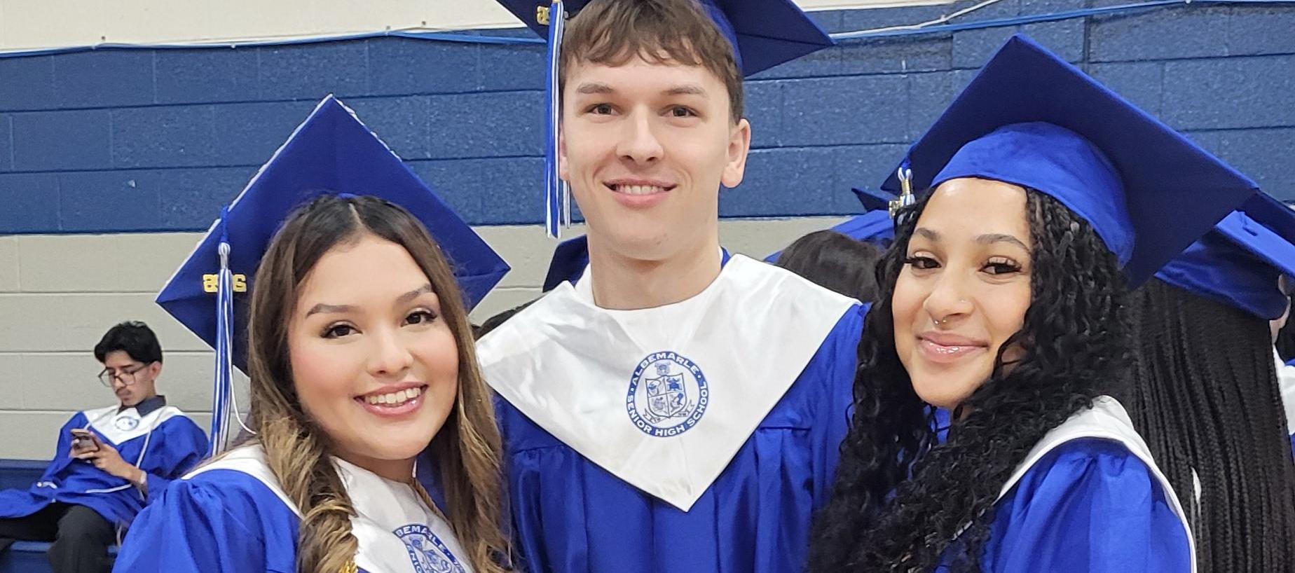 Three graduates in blue gowns pose together, showing their attire and accessories.