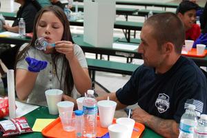 a girl blows a bubble into her had while a man watches