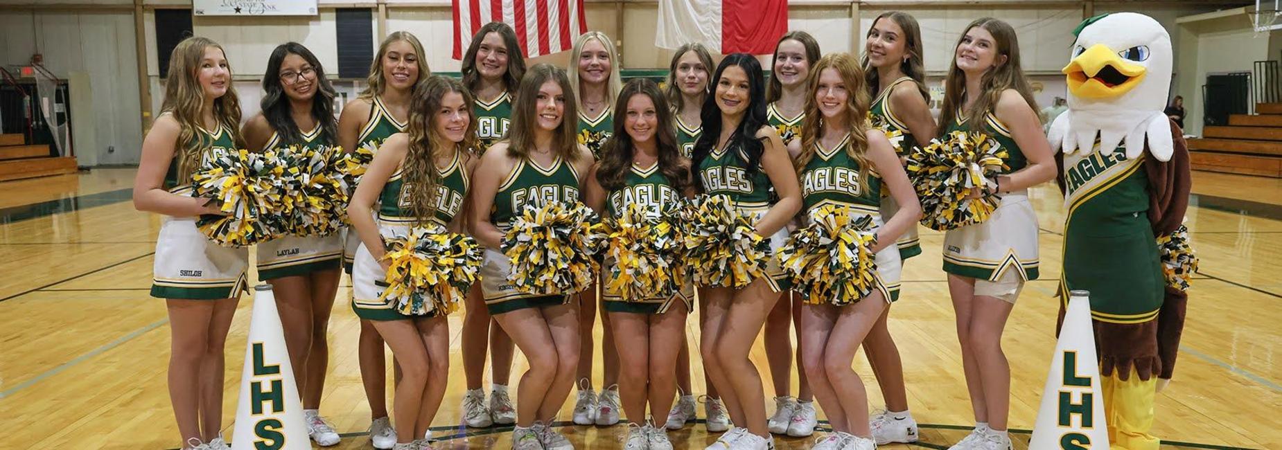 Group of cheerleaders in green and yellow uniforms posing with a mascot in a gym.