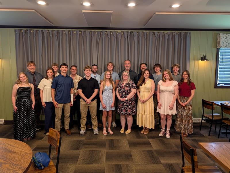 9 students and their guest teachers smiling at camera inside of restaurant