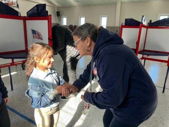 an elementary scholar smiles as she receives a "I Voted" sticker from a polling place worker on Election Day