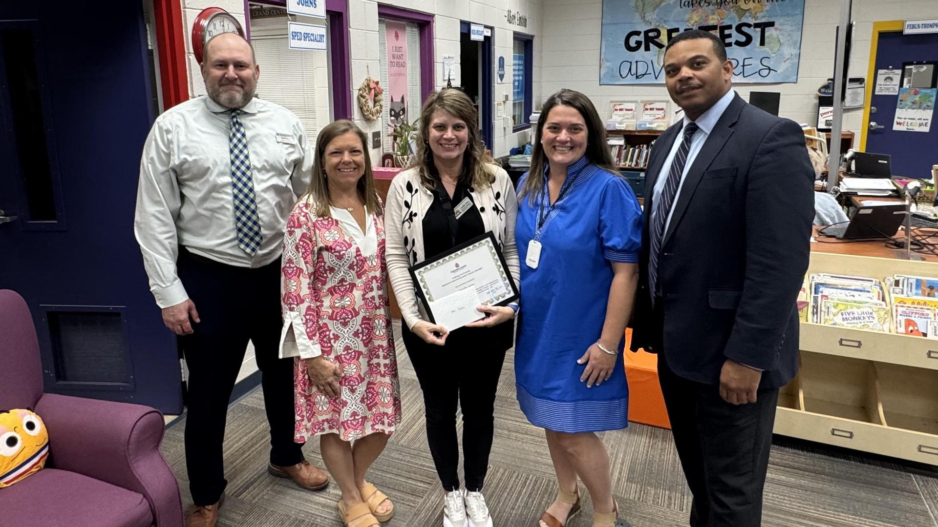 Five people standing together in a classroom, one holding a certificate.
