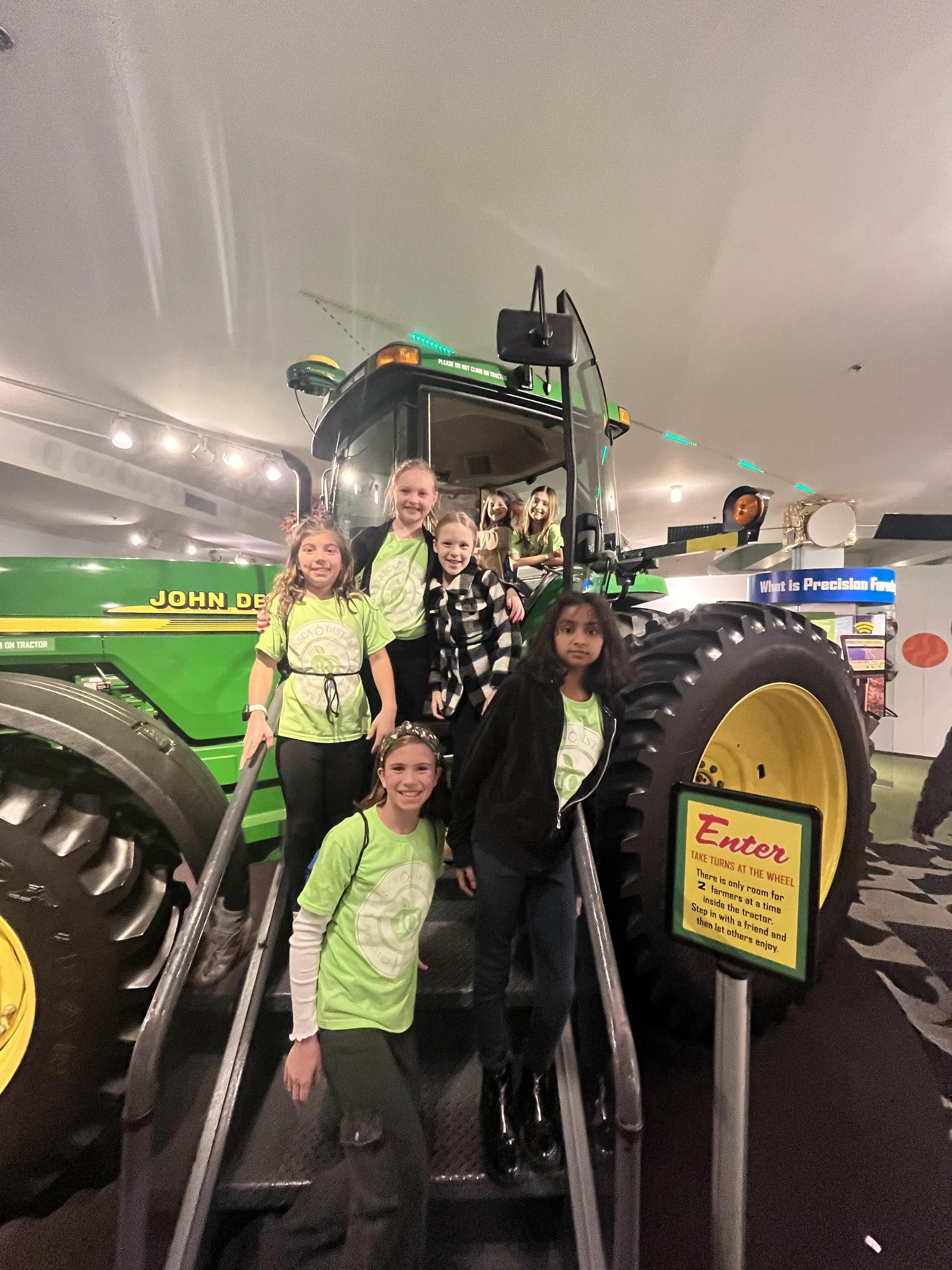 students posing in front of a tractor on a field trip