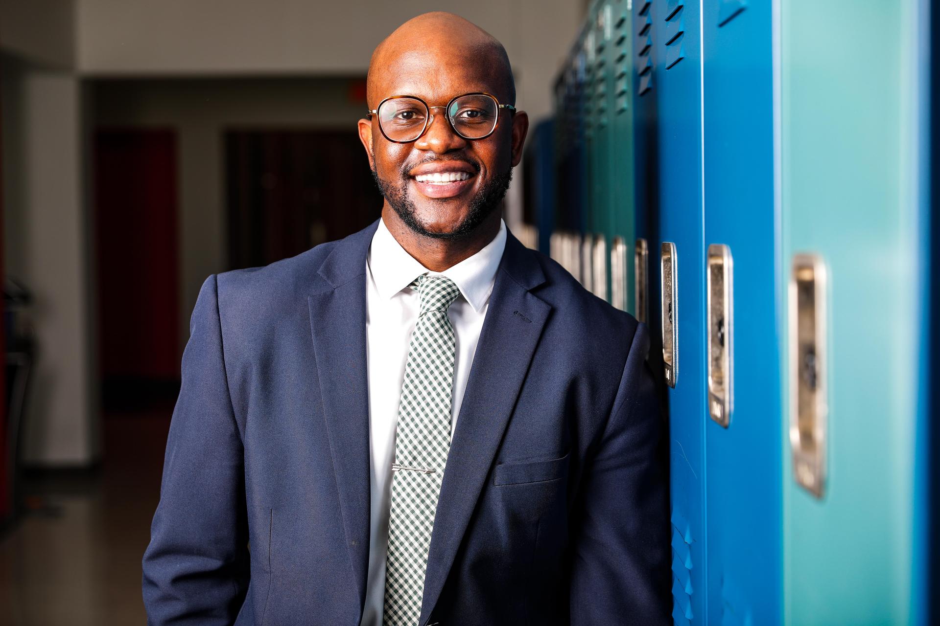 Middle school principal smiling in front of bushes.