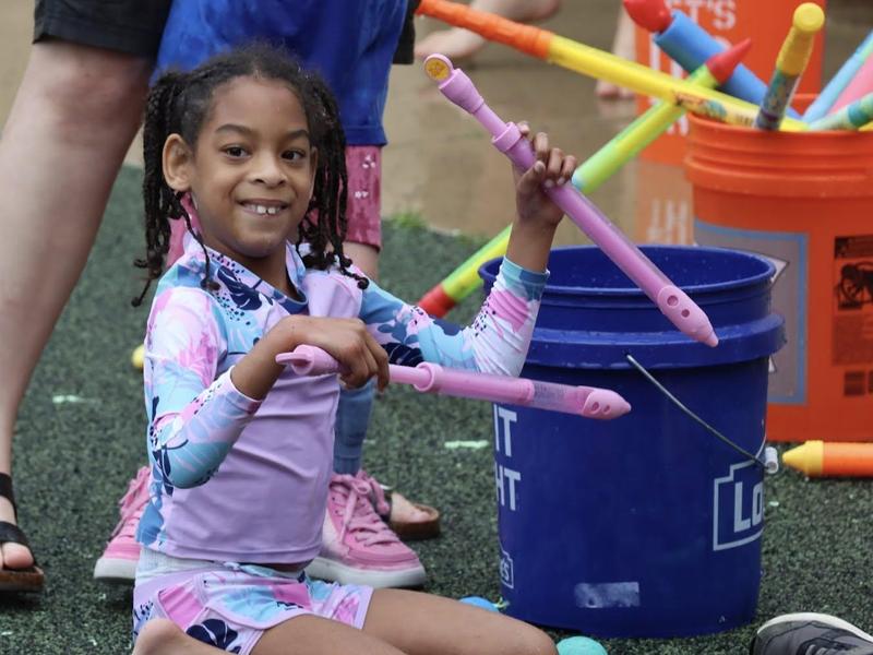 Child in swimwear holds colorful toy instruments while smiling.