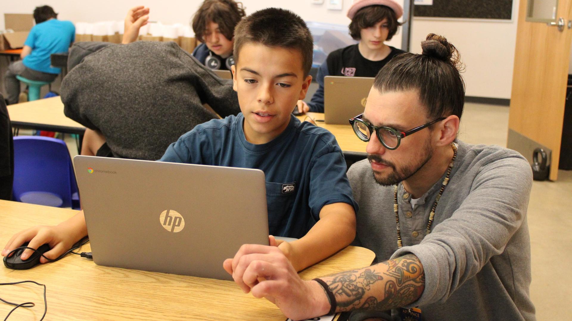 Boy working on a computer, teacher kneeling beside to help