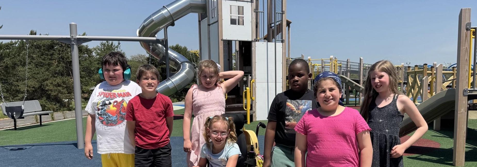 Group of children posing together at a playground with slides and play structures.