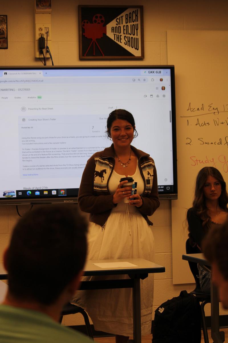 woman in dress holding coffee smiling at class in front of room