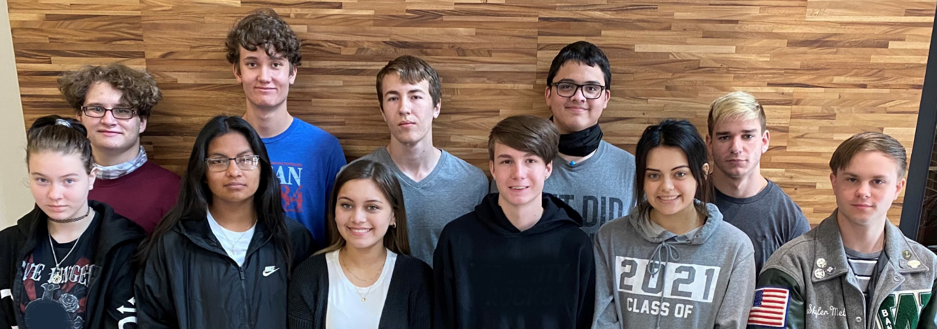 group of 11 teens standing in front of a wooden wall