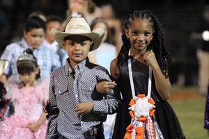 Two children, one in a cowboy hat and the other in a black dress, smiling at an event.
