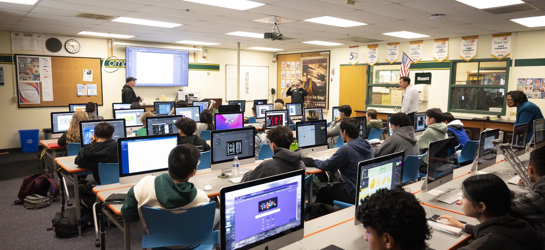 Students working on computers in a classroom with various resources on the walls.