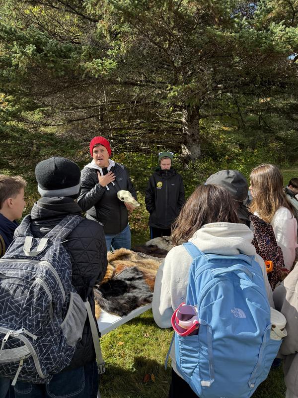 A presenter gestures while explaining to a group near animal fur displays.