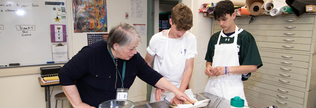 A teacher showing how to prepare dough for two students in a culinary arts class.