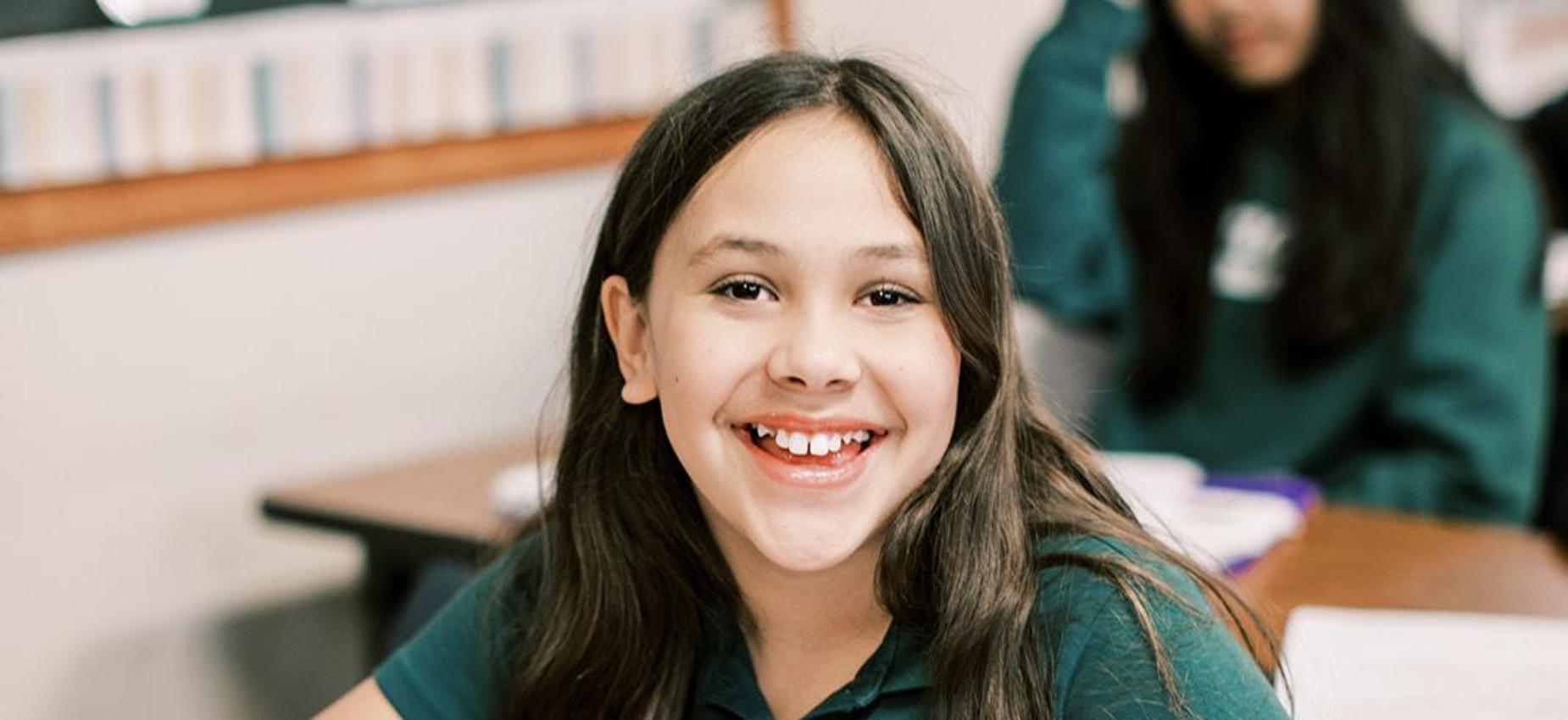 Smiling student sits at her desk with an open binder