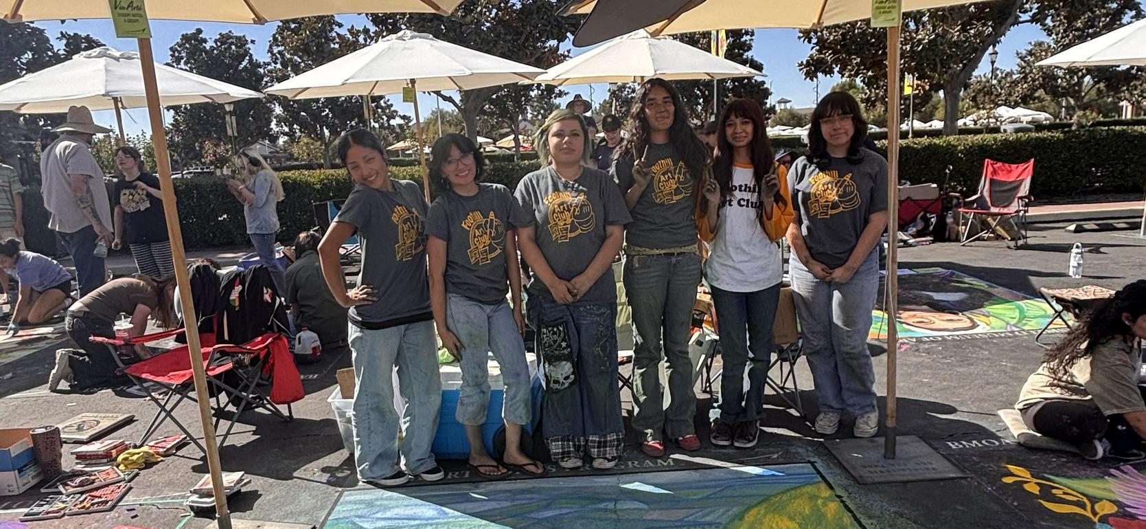 Group of six artists posing in front of their chalk art at an outdoor event.