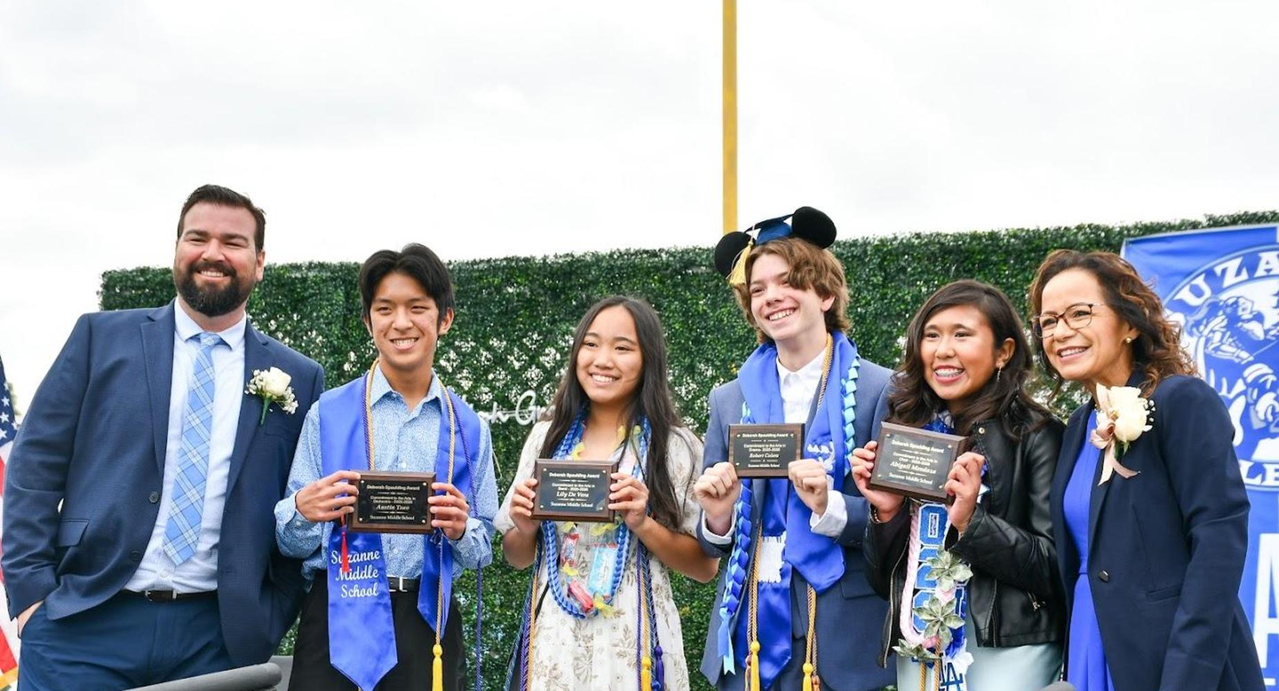 Group of graduates holding plaques at a ceremony outdoors.