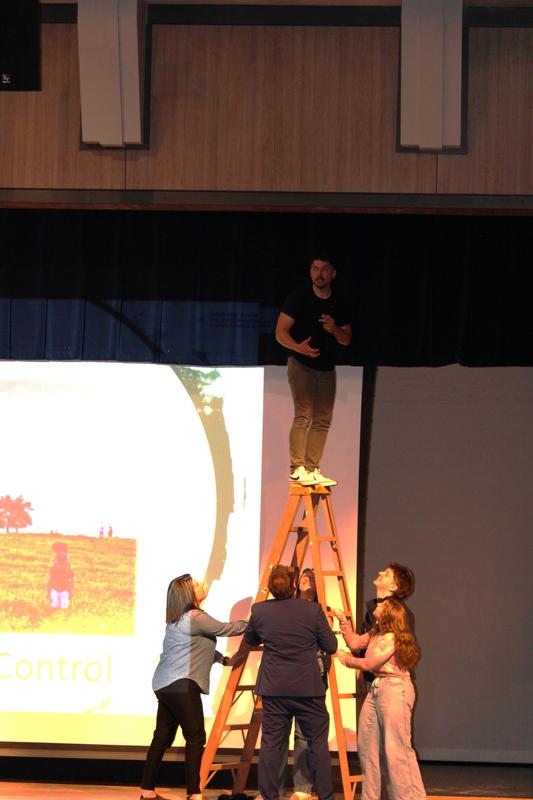speaker standing on ladder while community supports the ladder