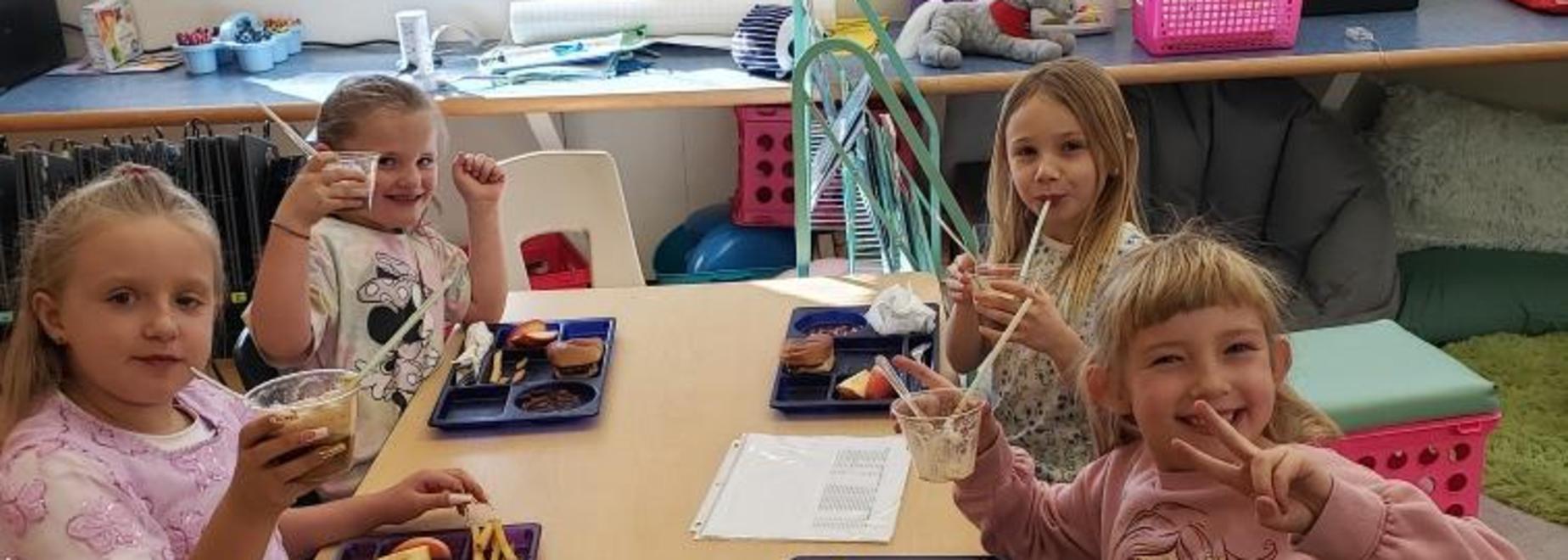 Group of four children enjoying lunch with food trays.