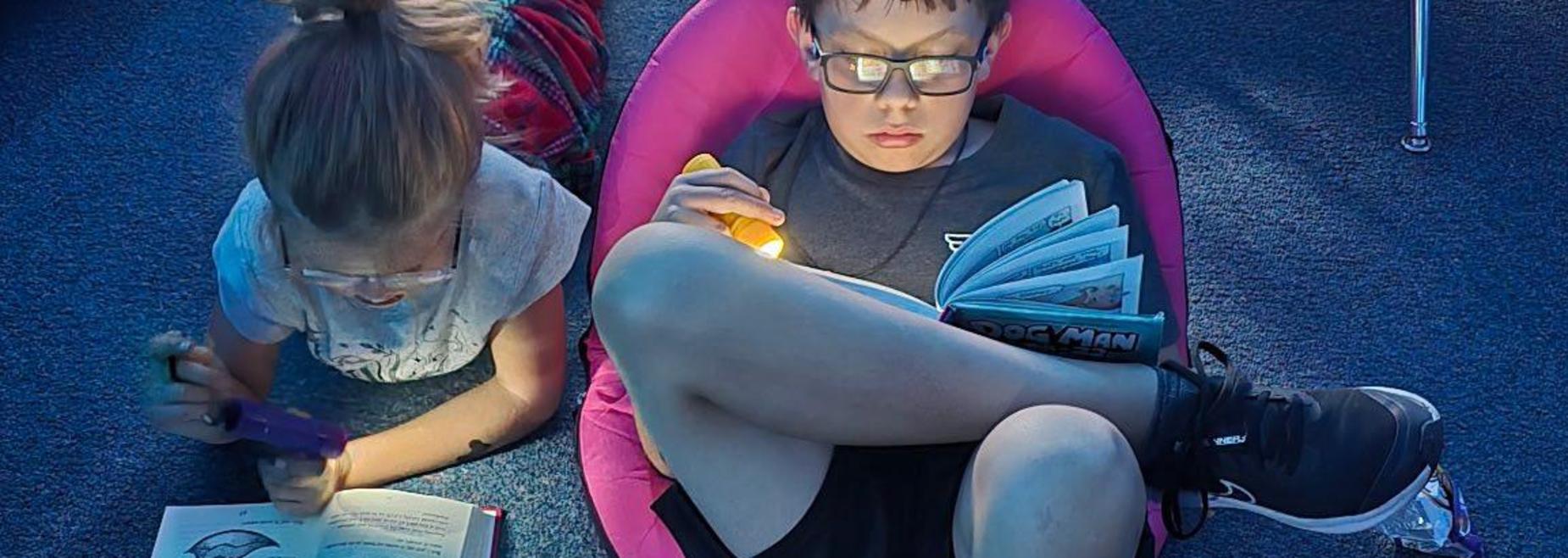 Children reading books in cozy chairs with flashlights in a soft-lit room.